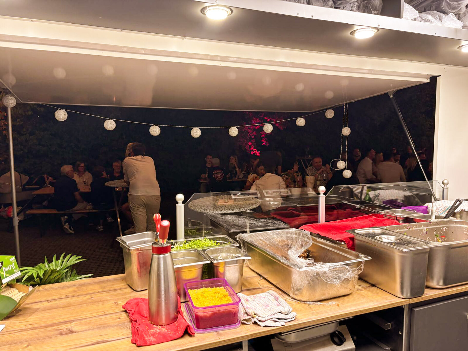 Buffet bei einem Abendevent mit Lichterketten und Gästen